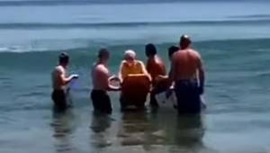 Fem mænd står ude i havet omkring en døende mand, og et øjeblik senere bryder al